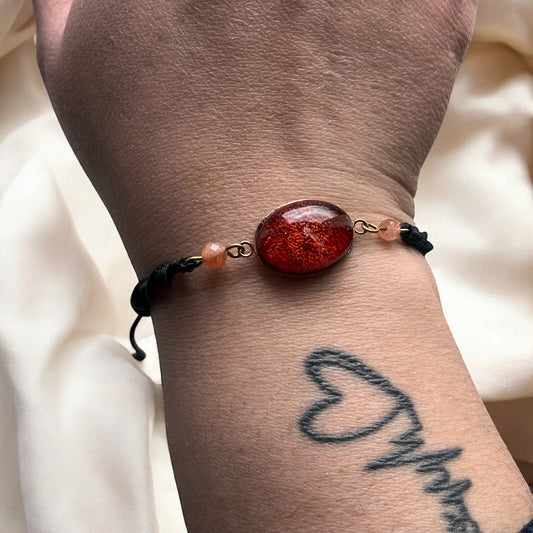 Bracelet en macramé noir, résine rouge et pierre de soleil – “Rouge Soleil”