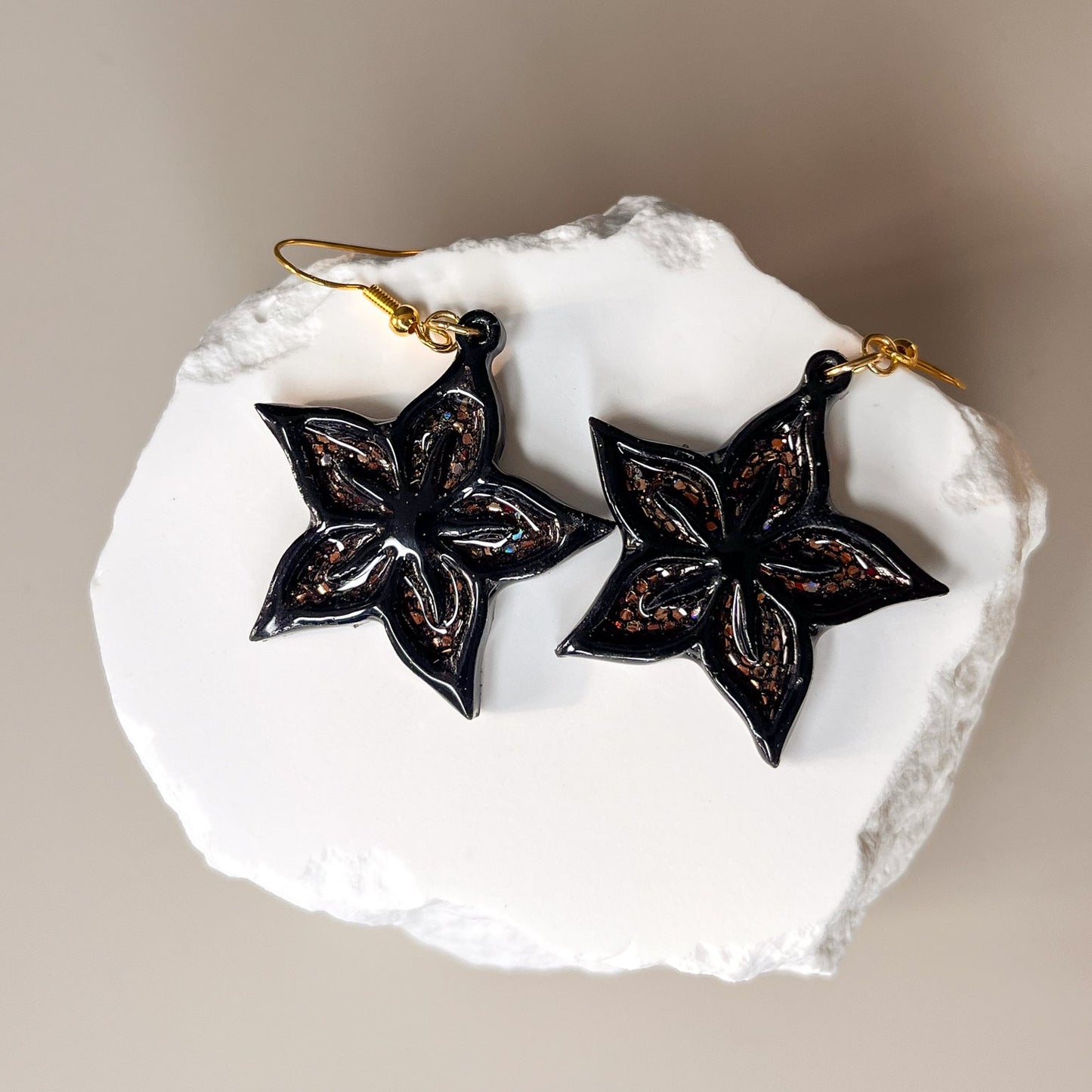 Boucles d’oreilles fleur étoilée en acrylique noir et résine cuivrée pailletée – Étoile assumée